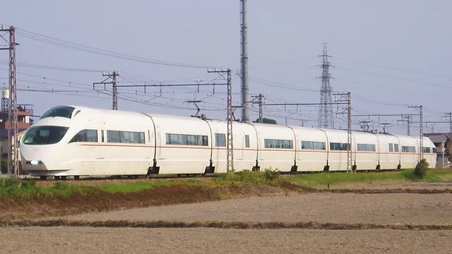A white limited express train crossing rural rice fields in Japan