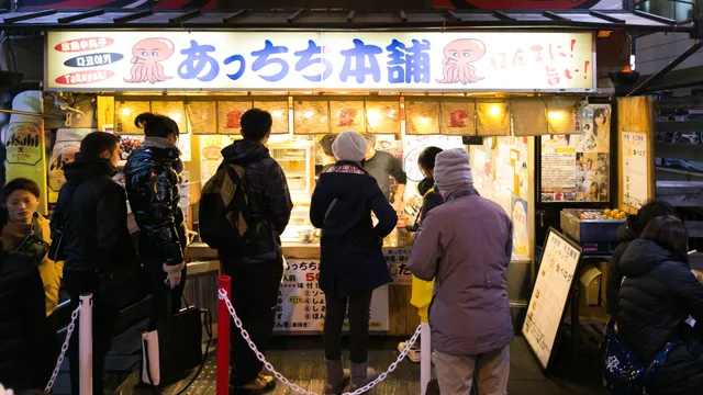 A takoyaki shop storefront with a queue of customers in Dotonbori, Osaka