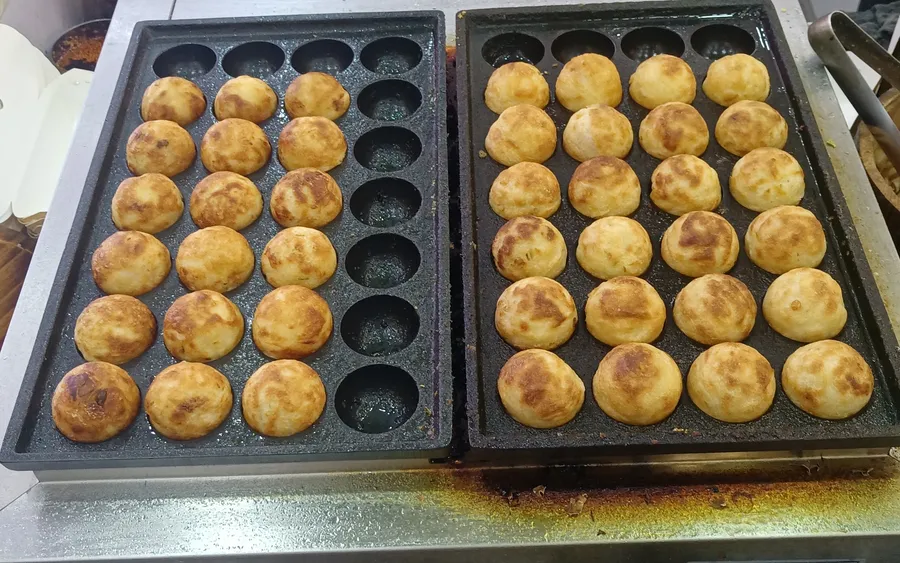 Rows of takoyaki cooking on a griddle