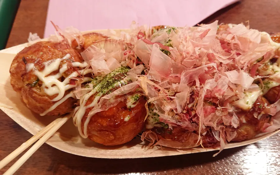 A tray of takoyaki topped with sauce, mayo, and bonito flakes